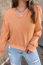 Woman in peach V-neck long sleeve waffle knit top, ribbed cuffs, jeans