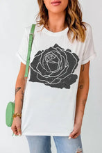 Women’s white t-shirt with black rose graphic, distressed jeans, green bag. Machine wash