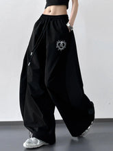Black wide leg drawstring pants with heart shaped embroidered patch on the thigh in a comfortable jogger style