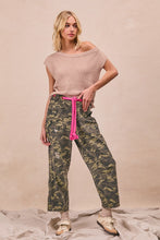 Camouflage print pants with relaxed fit, bright pink braided waistband, patch pockets, and denim material