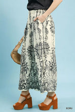 Cream-colored umgee border print wide leg pants featuring a black intricate baroque-style border print design
