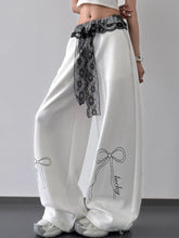 White satin wide leg pants with black lace belt trim and embroidered bow details featuring lucky text