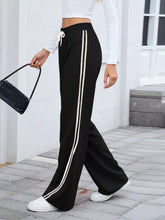 Black striped wide leg track pants with two vertical white stripes and a matching drawstring waistband