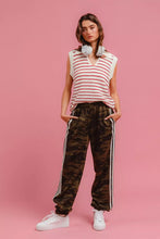 A woman wears BiBi side lines camouflage track pants in velour with black side stripes and a sleeveless striped knit vest