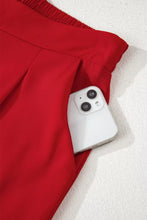 A sleek white smartphone in the side pocket of a red pleated skirt with high elastic waist detailing
