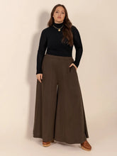 A woman wears plus size wide leg olive green pants with pockets paired with a black turtleneck top