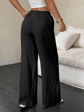 Black tied wide leg pants featuring pleated wide leg design and elastic waistband for comfortable wear