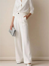Silver metallic clutch purse with minimalist design and subtle logo detail styled with high-waisted wide leg pants