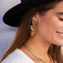 Woman in black hat and white top wearing 18k gold-plated heart earrings