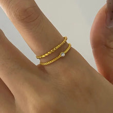 Two thin 18K gold-plated shell design rings on finger with clear stone