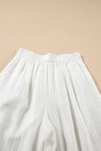White tie waist pleated wide leg pants made of lightweight textured fabric with elastic waistband