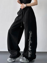 Black wide leg sweatpants with a loose fit drawstring waist and white cursive lettering down the side