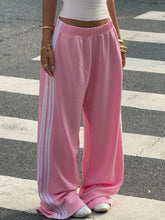Pink adidas wide leg pants featuring three white stripes down the side for a sporty stylish look