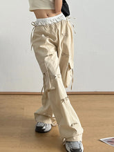 Beige cargo wide leg pants with drawstring waistband and decorative bow tie details at the pockets
