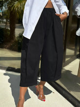 Black high-waisted wide leg pleated trousers with a relaxed flowing silhouette for elegant casual wear