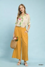 A woman wears umgee linen frayed side pocket mustard yellow wide leg pants with side slits paired with white sandals
