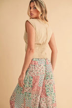 A woman wears aemi+co printed wide leg pants with floral patterns in soft pink green and cream tones and a beige top