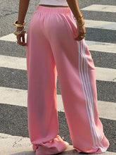 Pink adidas wide leg pants featuring three white stripes down the side for a sporty and comfortable fit