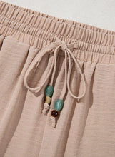 Beige casual wide-leg pants with gathered waistband and decorative beads on the drawstring tie for comfortable wear