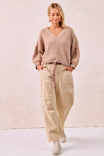 Beige ribbed knit v neck sweater with long sleeves and drawstring waist paired with striped twill barrel pants