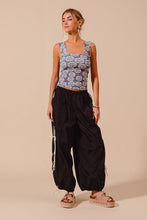 A woman wears black loose fit jogger pants with double lined side detail paired with a gray floral sleeveless top