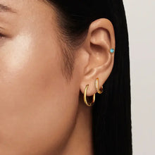Close-up of woman’s ear with three 18K gold-plated stainless steel earrings: two hoops and one studded