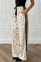 Cream-colored loose drawstring pants with leopard print abstract dots and black side stripe detail for casual wear