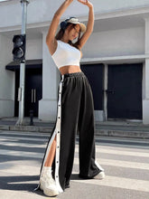 Black two-tone snap wide leg pants featuring white vertical stripe and button detailing along the side seam