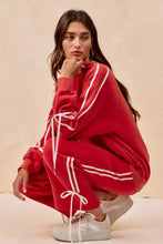 Red oversized sweatshirt with white striped lined bow details and matching drawstring ties complementing fleece sweatpants