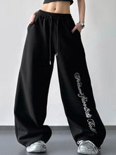 Black loose fit drawstring wide leg sweatpants with white cursive lettering down the side for casual wear