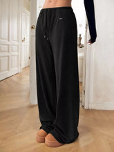 Black relaxed fit drawstring pants with wide leg soft flowing fabric and subtle logo on the waistband