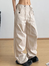 Beige relaxed wide-leg drawstring pants with black button details and cargo pockets for casual wear