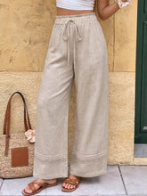 Beige linen casual wide leg pants with a drawstring waist and decorative lace trim at the hem