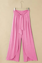 Pink high-waisted relaxed pants with knotted waist and split leg design featuring flowing wide-leg fabric