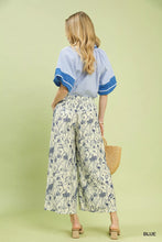 Woman wearing umgee two tone floral print pants in cream with navy botanical pattern paired with blue and white blouse