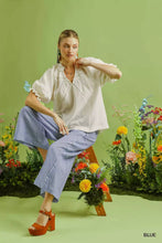Woman wearing umgee linen blend striped wide leg pants in blue with a white blouse featuring ruffled sleeves