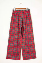 Red plaid wide-leg pants with black and white grid pattern hanging on wooden hanger showcasing plaid wide-leg pants