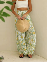 A woman wearing light green and yellow pineapple print drawstring paperbag waist wide leg pants with elastic waistband