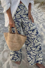 Beige woven straw tote bag with natural fiber handles paired with leaf print wide leg pants