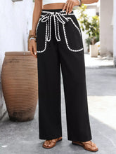 Black wide-leg trousers with white crochet trim tie waist and embroidered accents on waistband and pockets