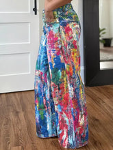 Vibrant wide leg denim pants featuring a bold abstract paint-splatter pattern in blues pinks reds and greens