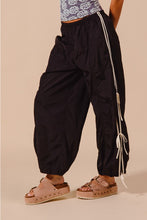 Black loose fit jogger pants with white vertical stripes and tassels along double lined side detail seam