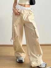 Beige cargo wide leg pants with a shiny satin finish and decorative bow tie details at the side pockets