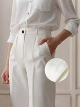White high-waisted wide leg pants with pleated tailored design and black button closure for a sleek look