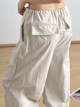 Beige relaxed wide-leg drawstring pants with elastic waistband and visible front pocket in loose-fitting cargo style