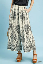 Cream-colored umgee border print wide-leg pants with intricate black floral paisley pattern elastic waistband pockets
