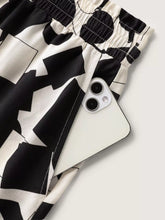 A white iphone peeking from the pocket of plus size black-and-white abstract print wide-leg pants