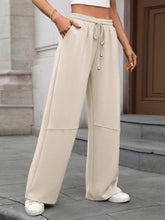 Beige drawstring high waist wide leg casual pants with elastic waistband and relaxed fit featuring subtle paneling