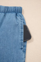 Blue chambray pants with an elastic waistband, ruffled hem, wide leg, and a smartphone in the side pocket
