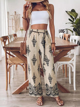 Beige high-waisted boho print wide leg pants with black intricate lace-like patterns and drawstring waistband